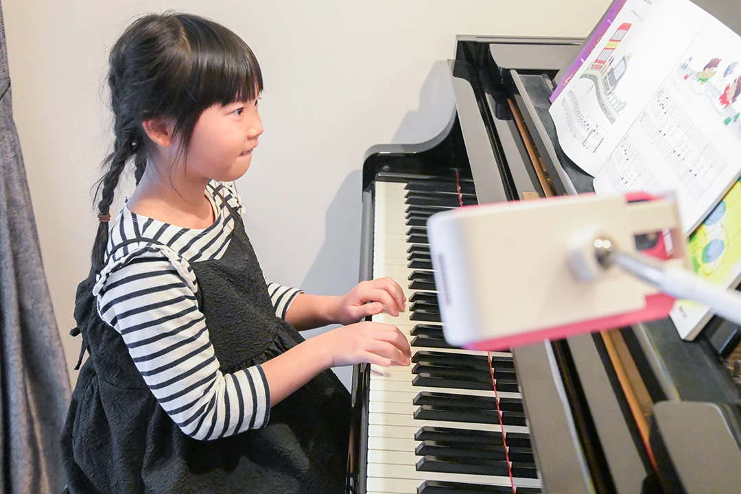 自宅のピアノでオンラインレッスンを受ける子ども