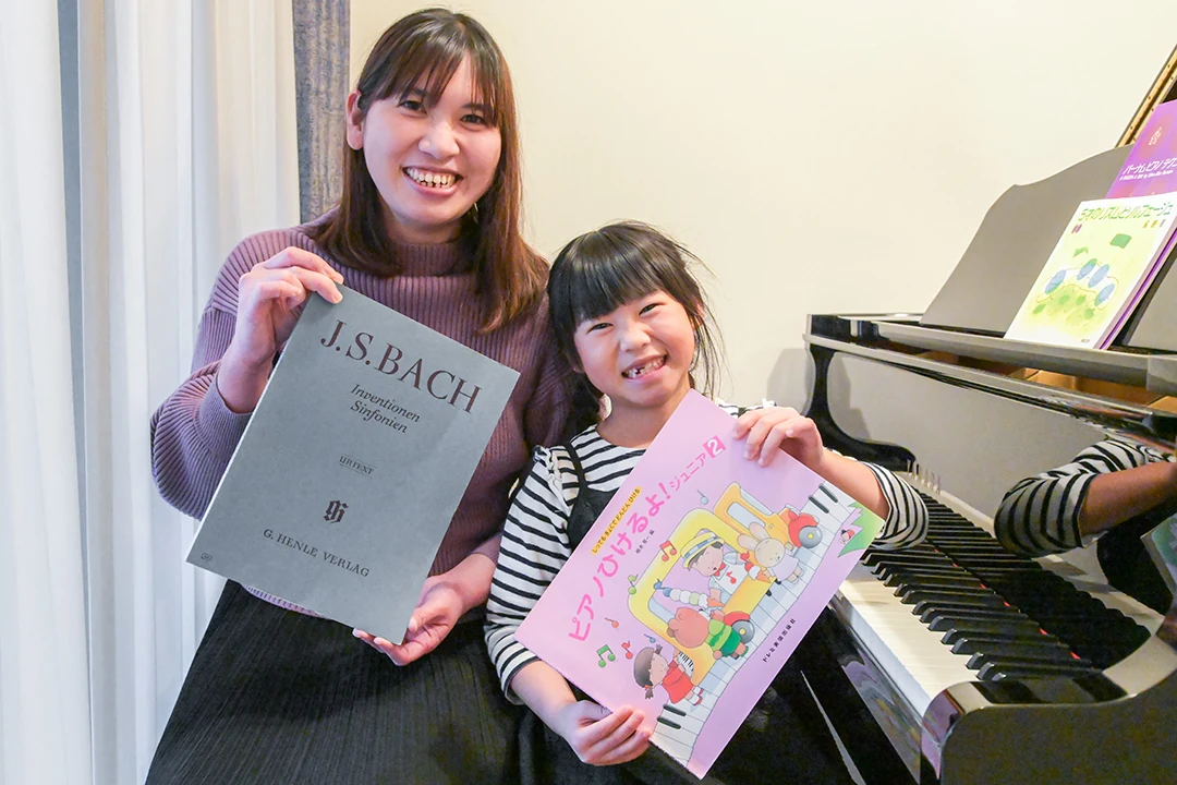 ピアノ教材を手に笑顔を見せる生徒と保護者